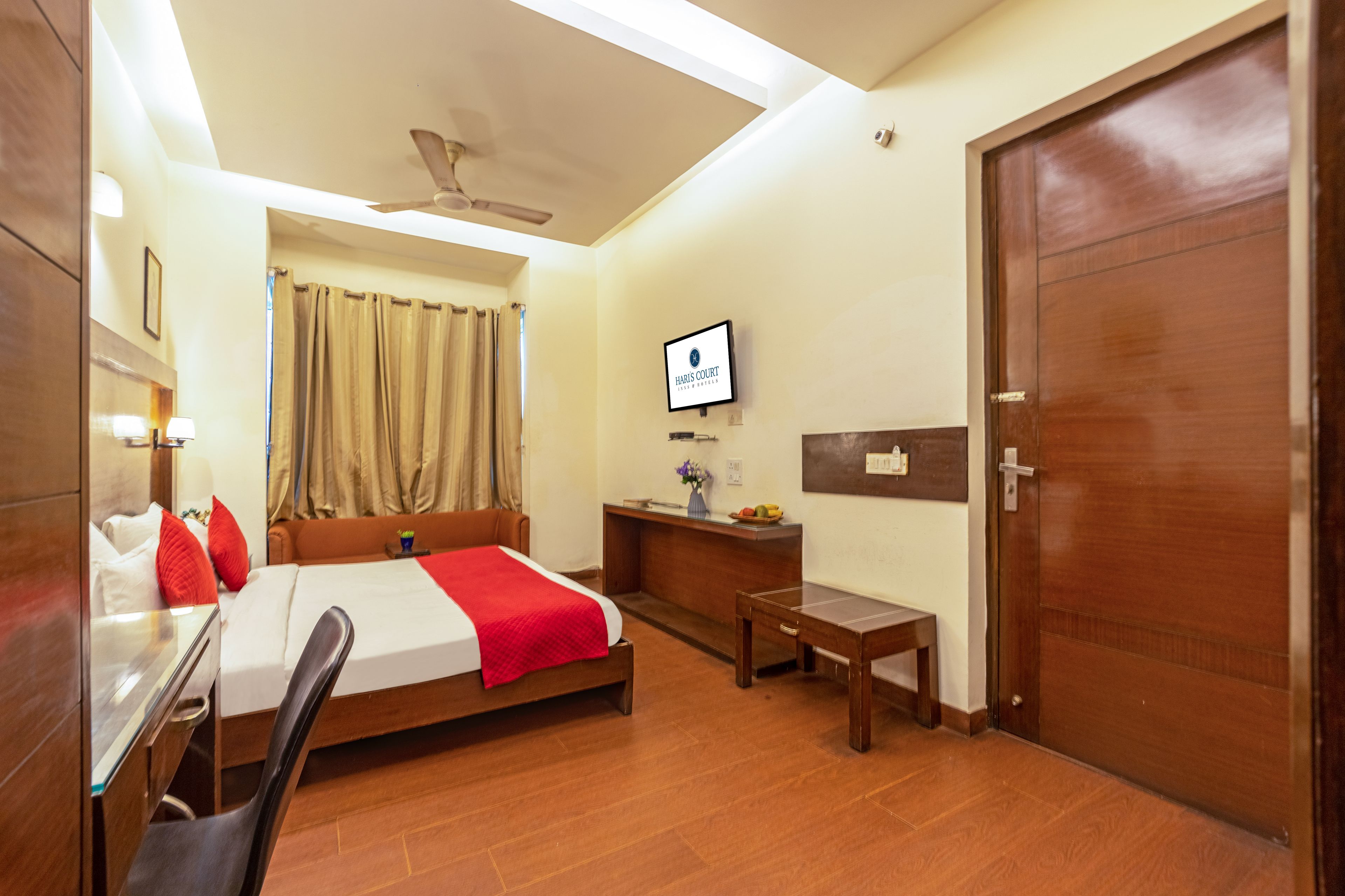 Une chambre d’hôtel avec un lit, un bureau, une chaise et un téléviseur fixé au mur.