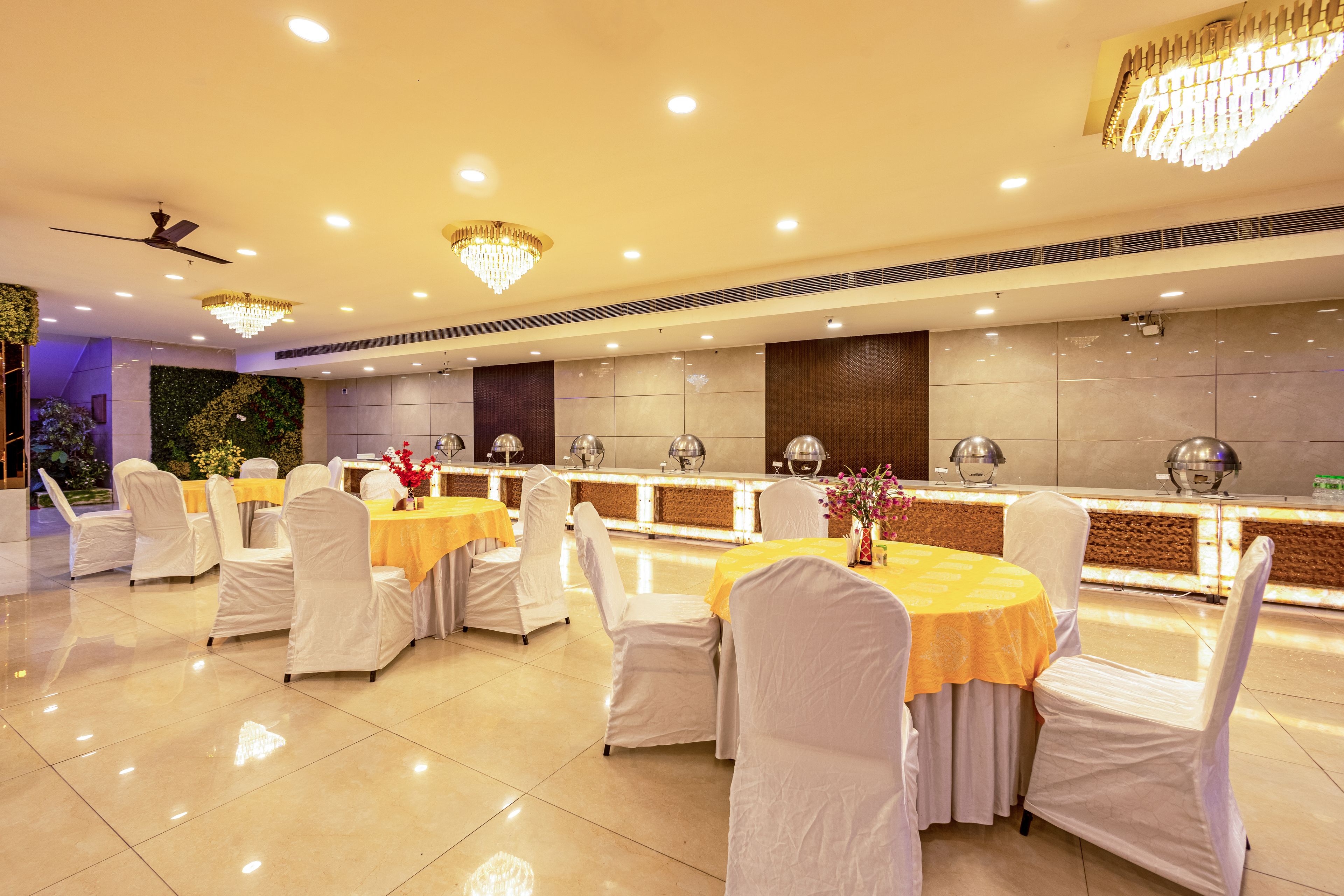 Una sala banchetti con tavoli rotondi, sedie bianche e un'area buffet centrale.