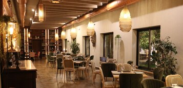 Un restaurante con mesas y sillas de madera, lámparas colgantes y vistas al exterior con vegetación.