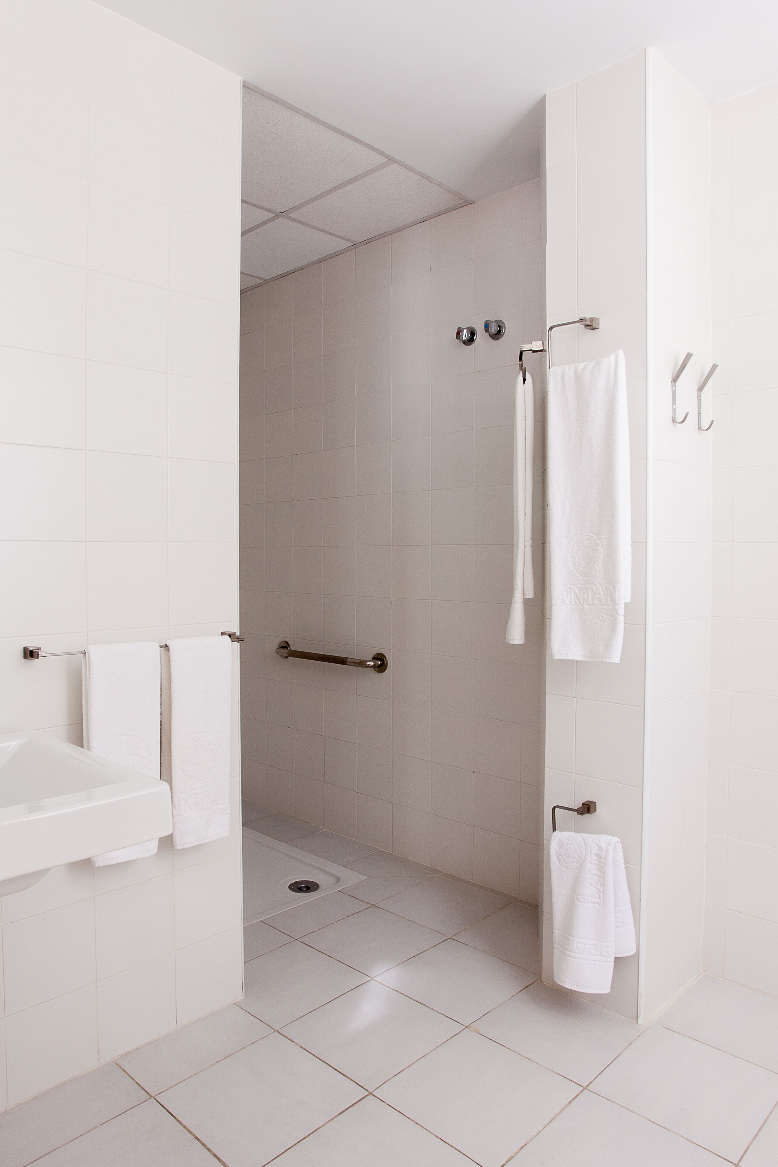 A modern bathroom with white tiles, a shower area, and a sink with a towel rack.
