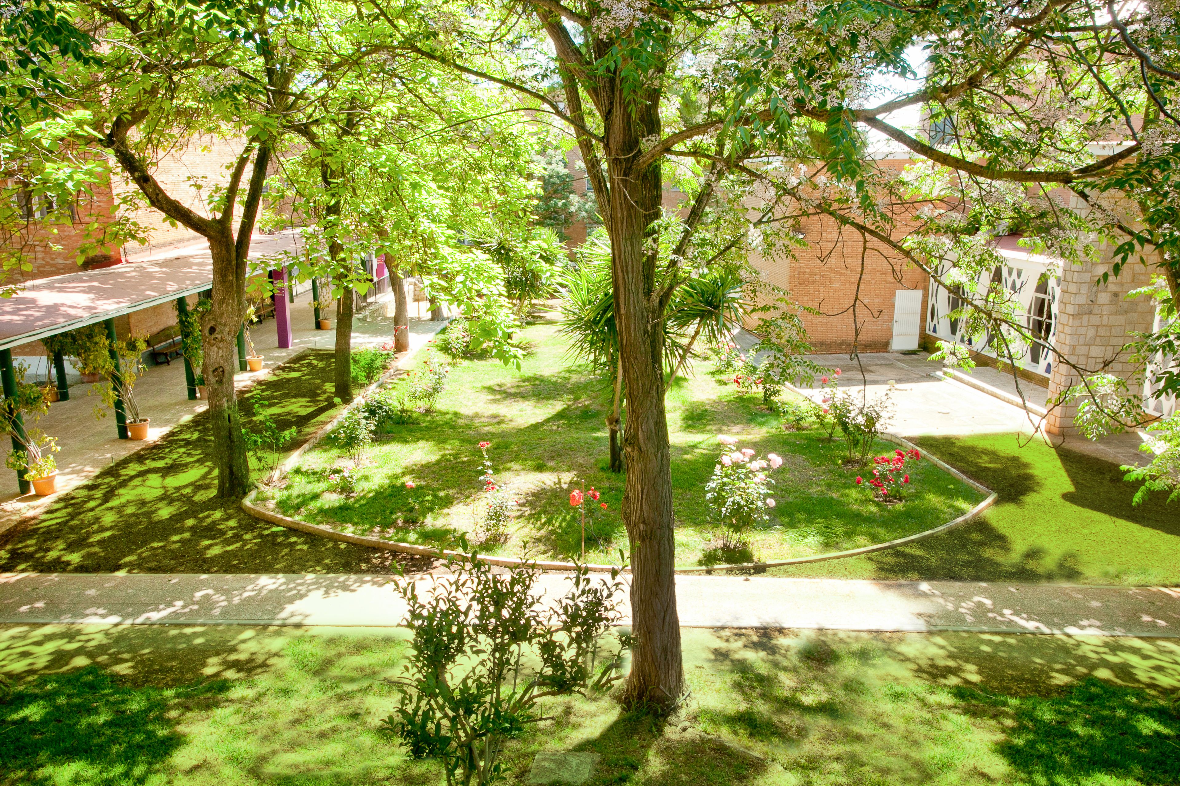 Un patio central con un árbol, rodeado por un edificio de ladrillo con un corredor cubierto.