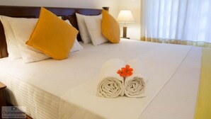A neatly made bed with white and yellow pillows, a rolled towel with a flower, and a bedside lamp. - Clovefield Villa (Hatton)