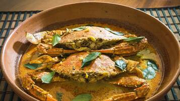 A clay pot containing a seafood dish with crab, likely a curry, garnished with bay leaves.