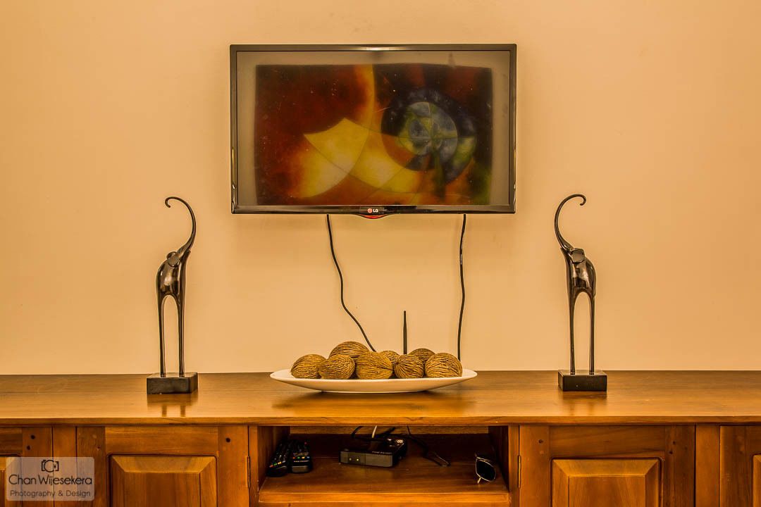 A television mounted on a wall above a wooden cabinet with a plate of balls and two decorative metal sculptures.