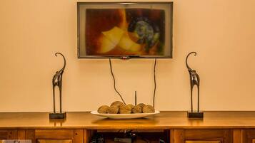 A television mounted on a wall above a wooden cabinet with a plate of balls and two decorative metal sculptures.
