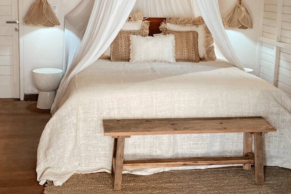 A bedroom with a canopy bed, a wooden bench, and two wall-mounted lamps.