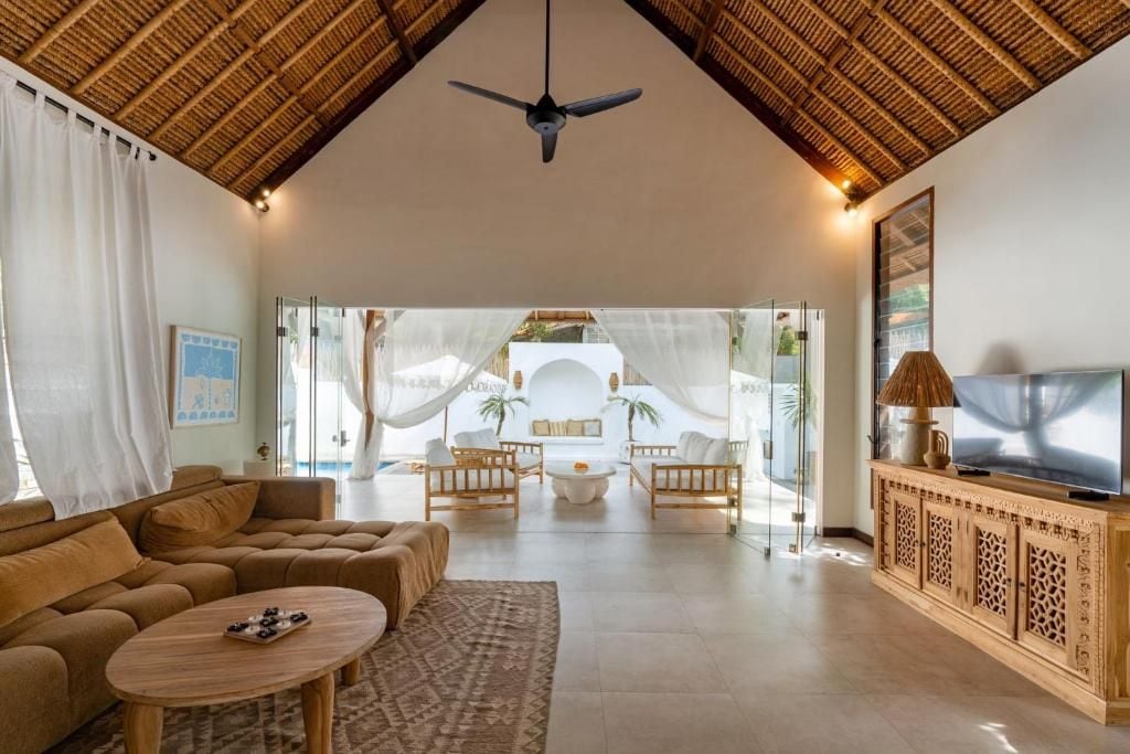 Ein großzügiger Wohnbereich mit hoher Decke, einem Deckenventilator, einer Sofagarnitur, einem Couchtisch und einem Fernseher auf einer Holzvitrine.