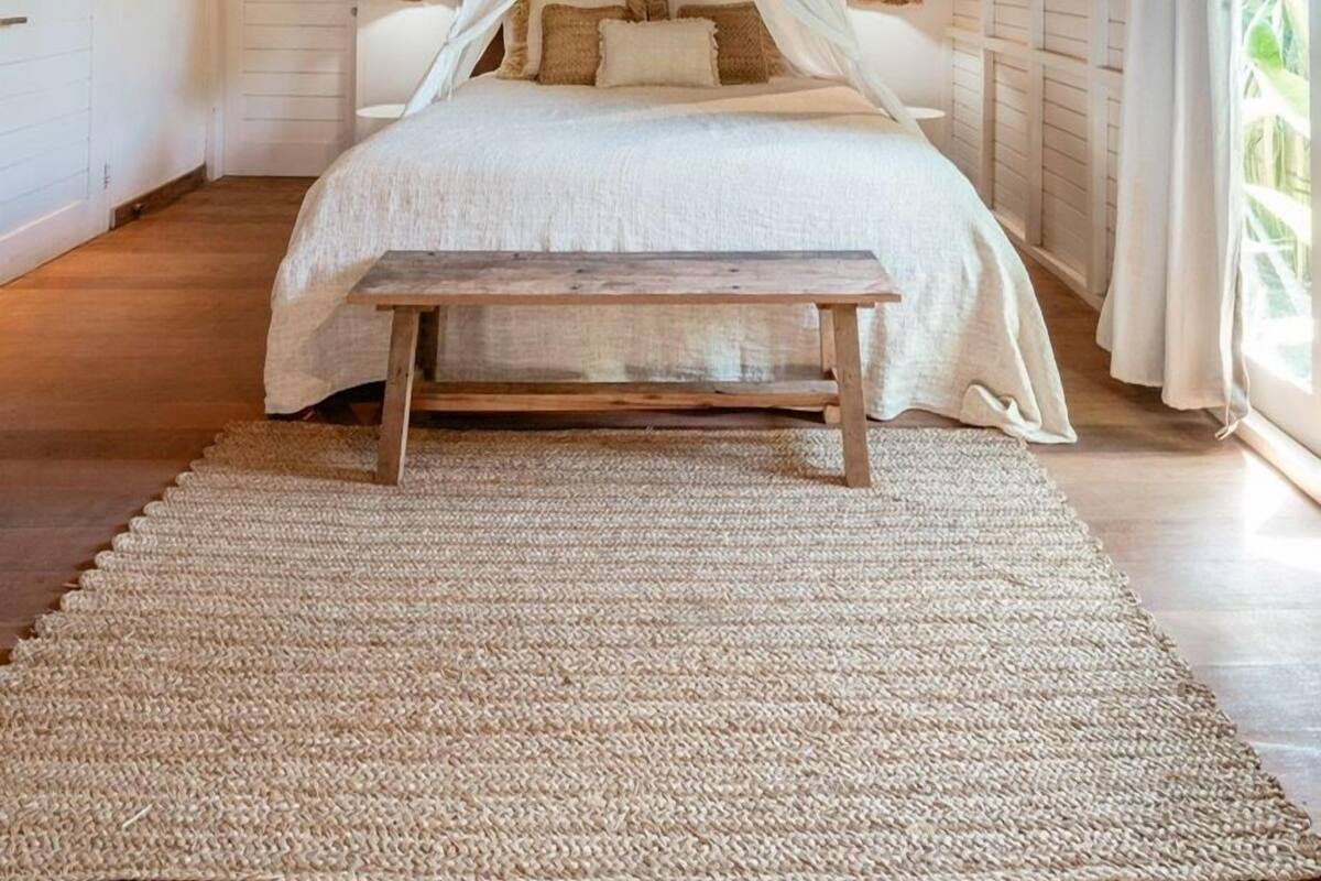 A bedroom with a wooden ceiling, a bed with a canopy, a wooden bench, and a woven rug.