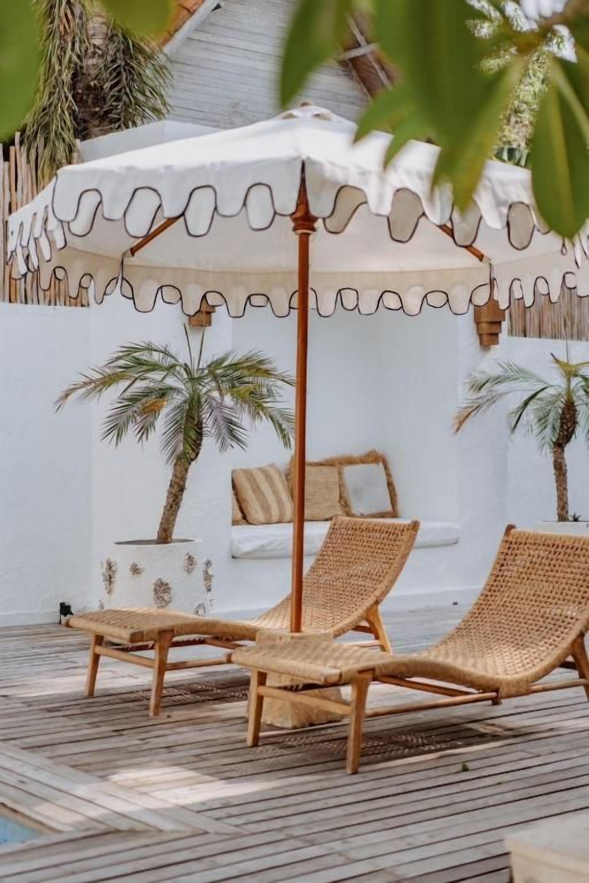 A sun lounge with two wicker chairs and a white umbrella.