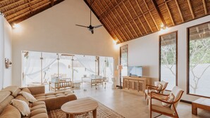 A spacious living area with a high ceiling, a ceiling fan, and large windows offering views of greenery. - Castaway Resort (Lembongan Island)
