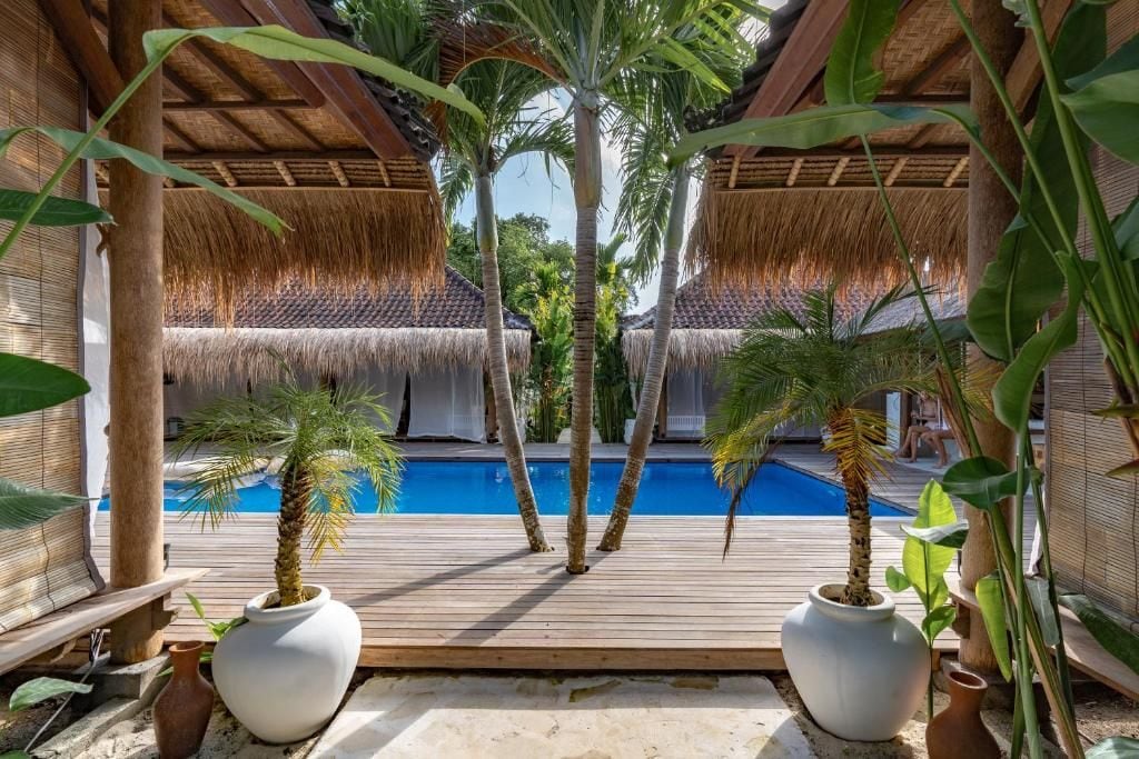A pool area with thatched roofs and potted palm trees.