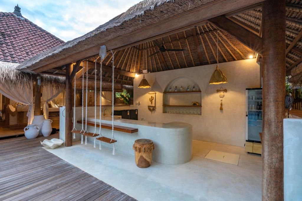 Un espace bar situé au bord de la plage, doté d’un toit de chaume, de poutres en bois et de lampes suspendues.