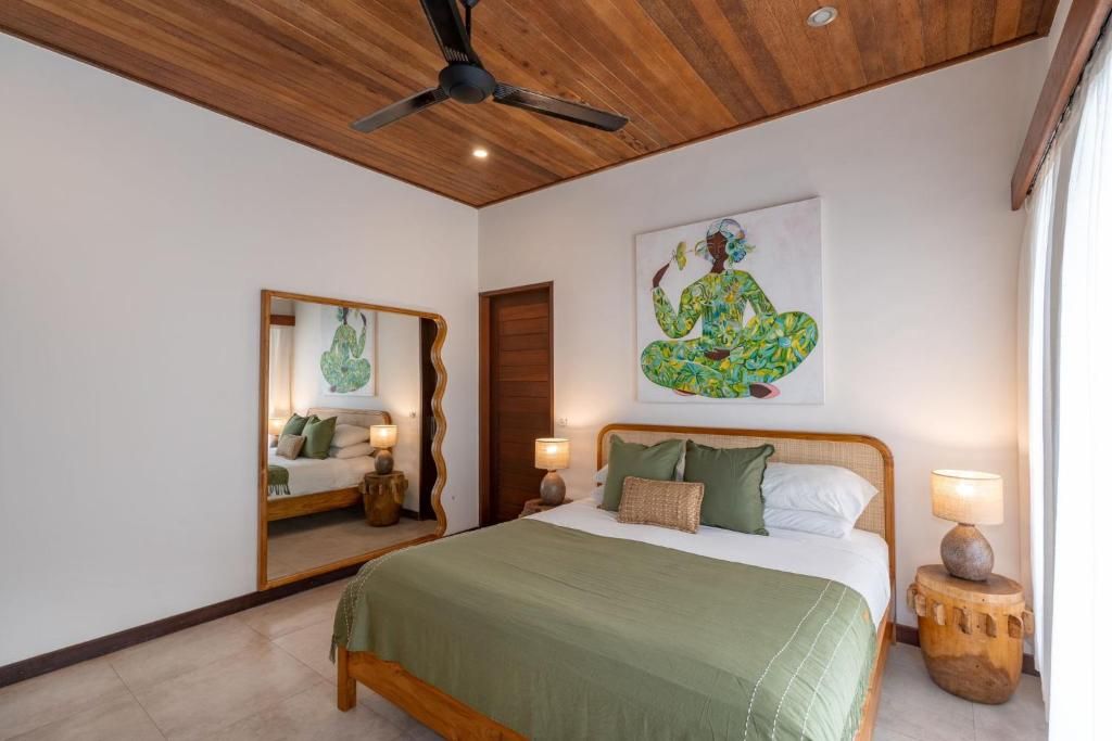 A bedroom with a bed, a ceiling fan, a mirror, and a painting on the wall.