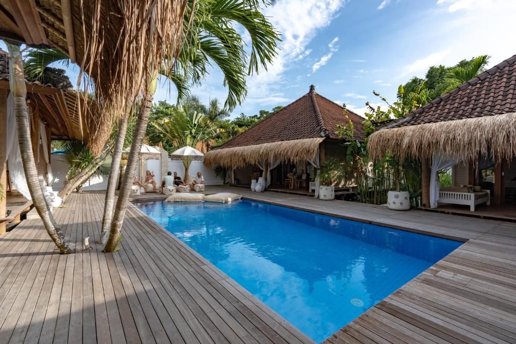 Une terrasse en bois avec une piscine, des constructions à toits de chaume et des palmiers.