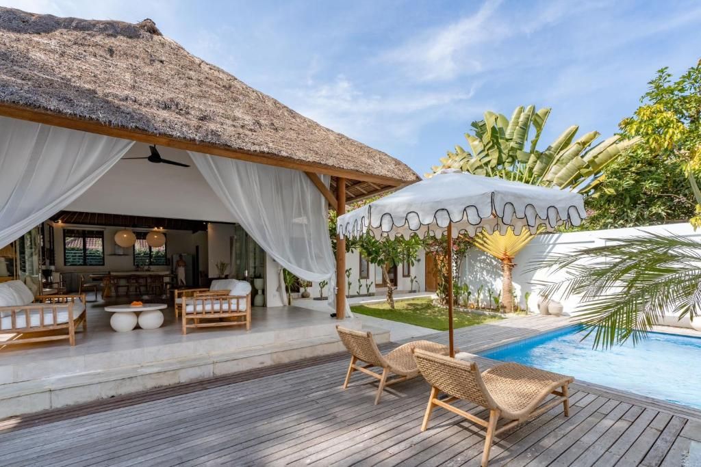 Un espace aménagé au bord de la piscine, doté d’une structure à toit de chaume, de chaises longues et d’une piscine.