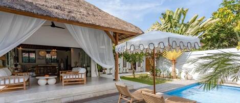 A poolside area with a thatched roof structure, lounge chairs, and a pool.