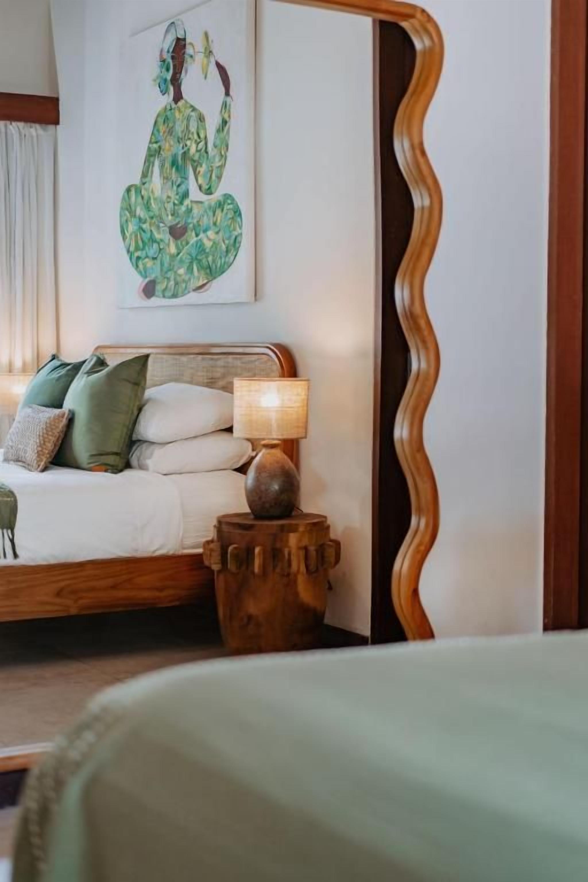 Een slaapkamer met een bed, kussens, een bedlampje en een kunstwerk aan de muur.
