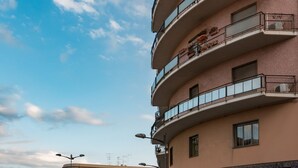 Un edifici d'àmbit múltiples pisos amb balcons, un carrer amb cotxes aparcats i un cel serè.