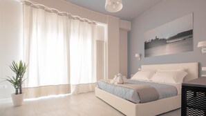 Un dormitori amb un llit, una planta en test, un quadre a la paret i una finestra amb cortines.