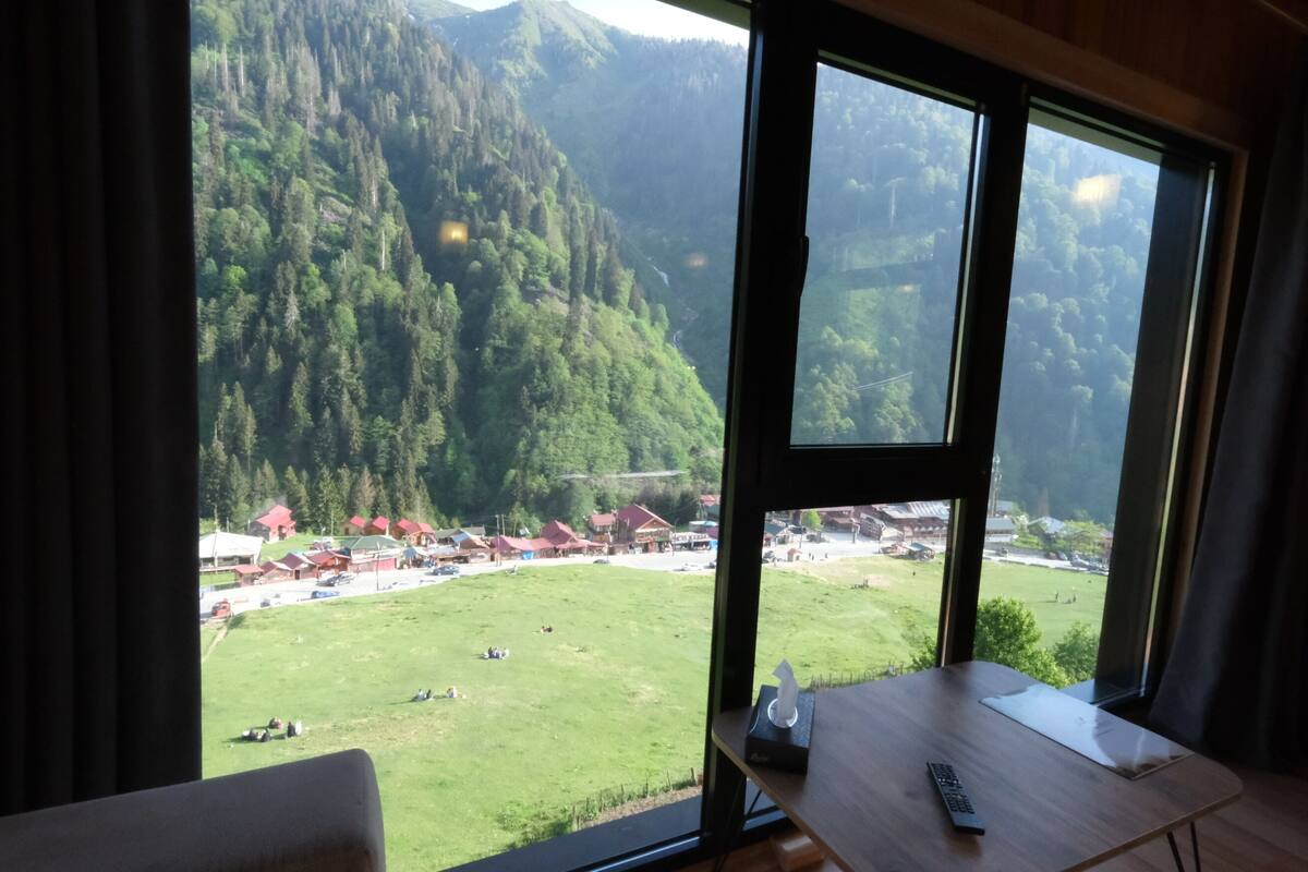 Une pièce dotée d’une grande fenêtre donnant sur un paysage montagneux et un village situé en contrebas.