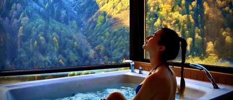 Una donna seduta in una vasca da bagno con vista su una foresta attraverso una finestra.