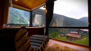 Een kamer met een groot raam dat uitkijkt op een bergachtig landschap.