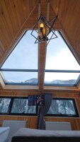 A room with a sloped ceiling, wooden beams, a skylight, a television screen, and a view of snow-capped mountains.