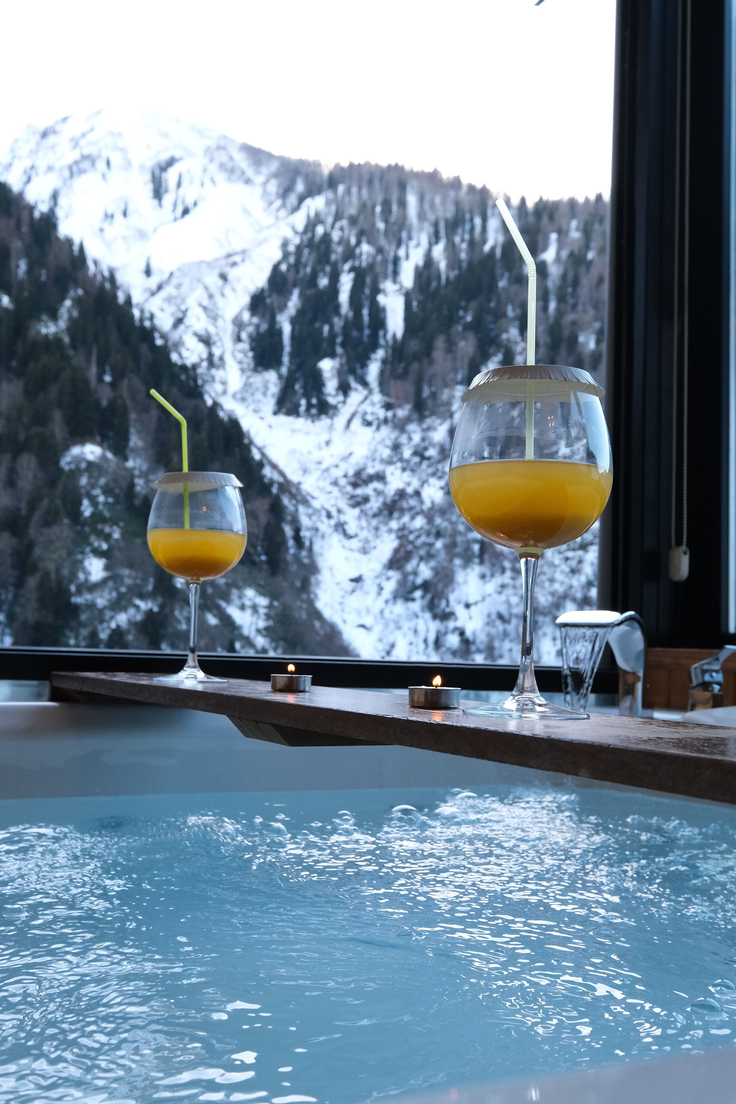 Two glasses of orange juice on a wooden ledge with a mountain view in the background.