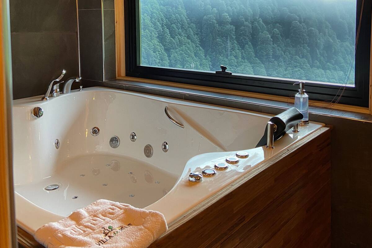 L’intérieur d’un chalet en bois, avec une grande baignoire, une fenêtre donnant sur la forêt et une serviette posée sur le bord.