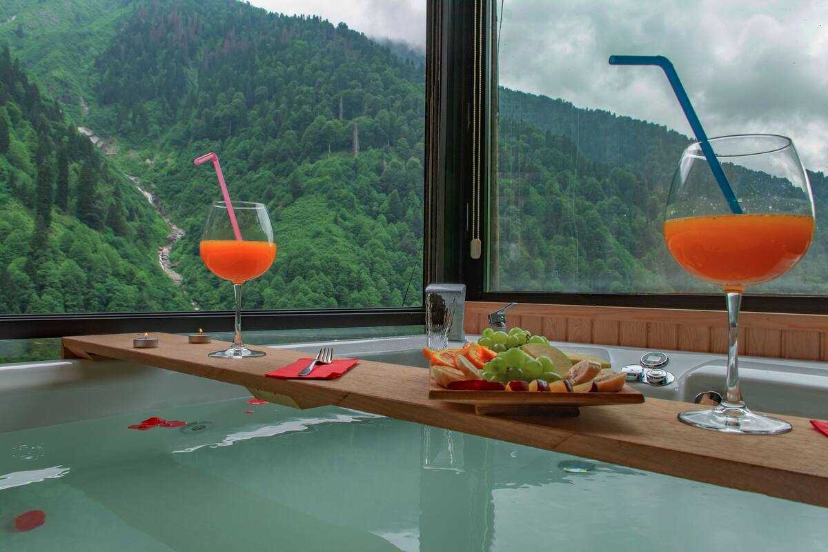Une table en bois avec deux verres de jus d’orange, une assiette de fruits et une bougie.