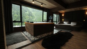 Een moderne kamer met een houten vloer, een groot houten bureau met een computer, een bank en een groot raam met uitzicht op een bos.