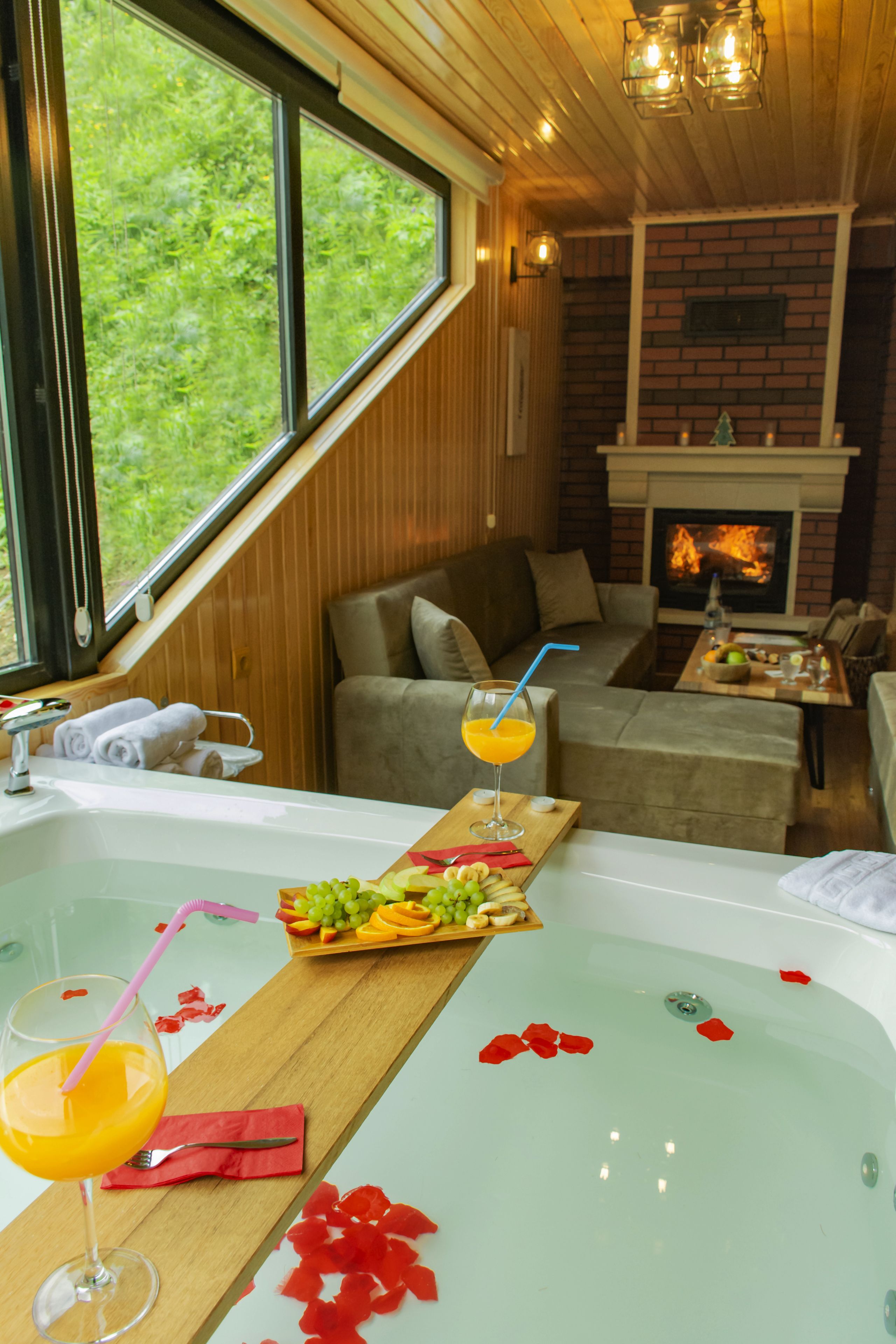 A room with a large bathtub, a fireplace, a sofa, and a dining table with fruit and drinks.