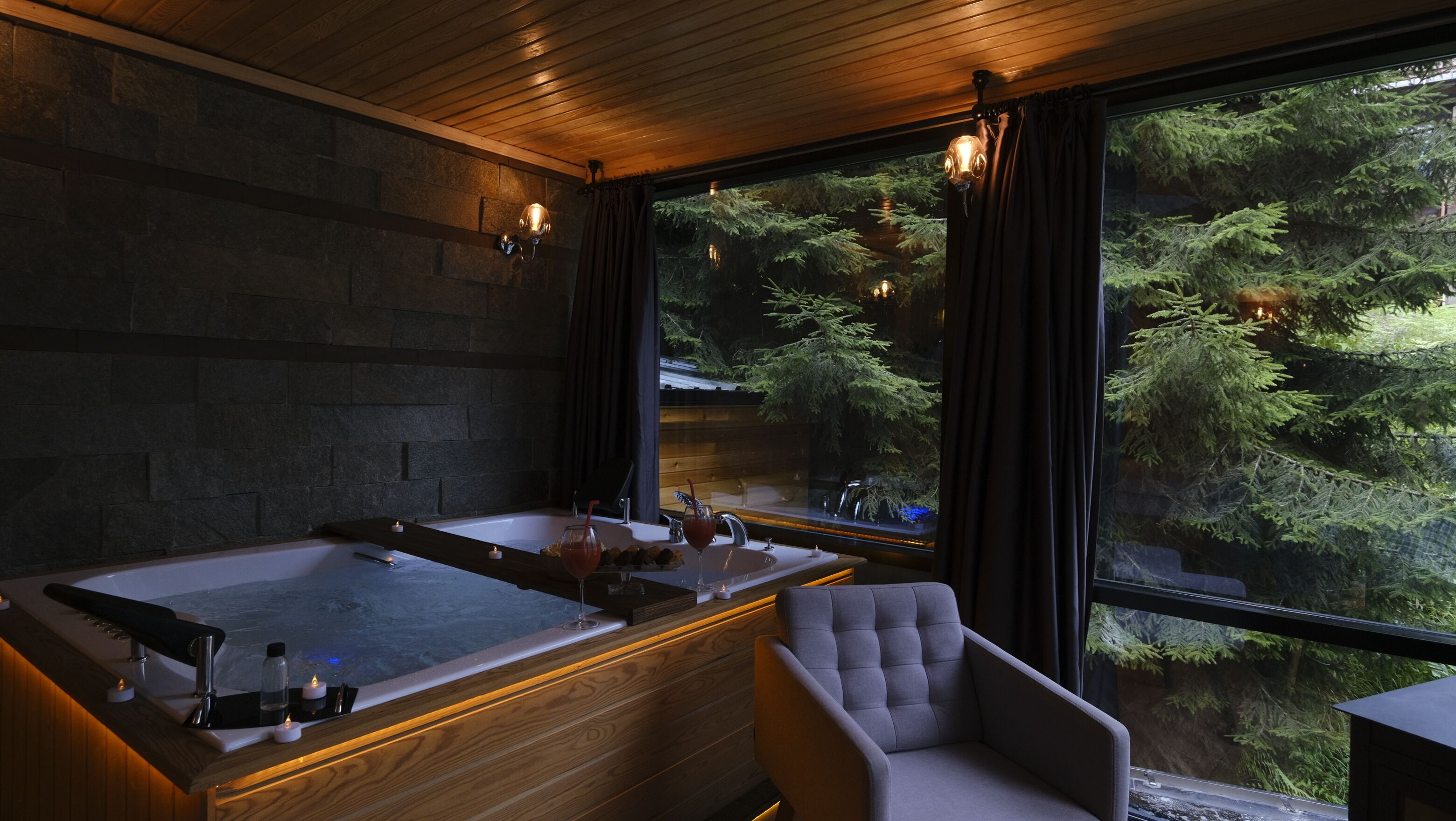 A modern bathroom with two large tubs, a wooden vanity, and a view of a forest through large windows.