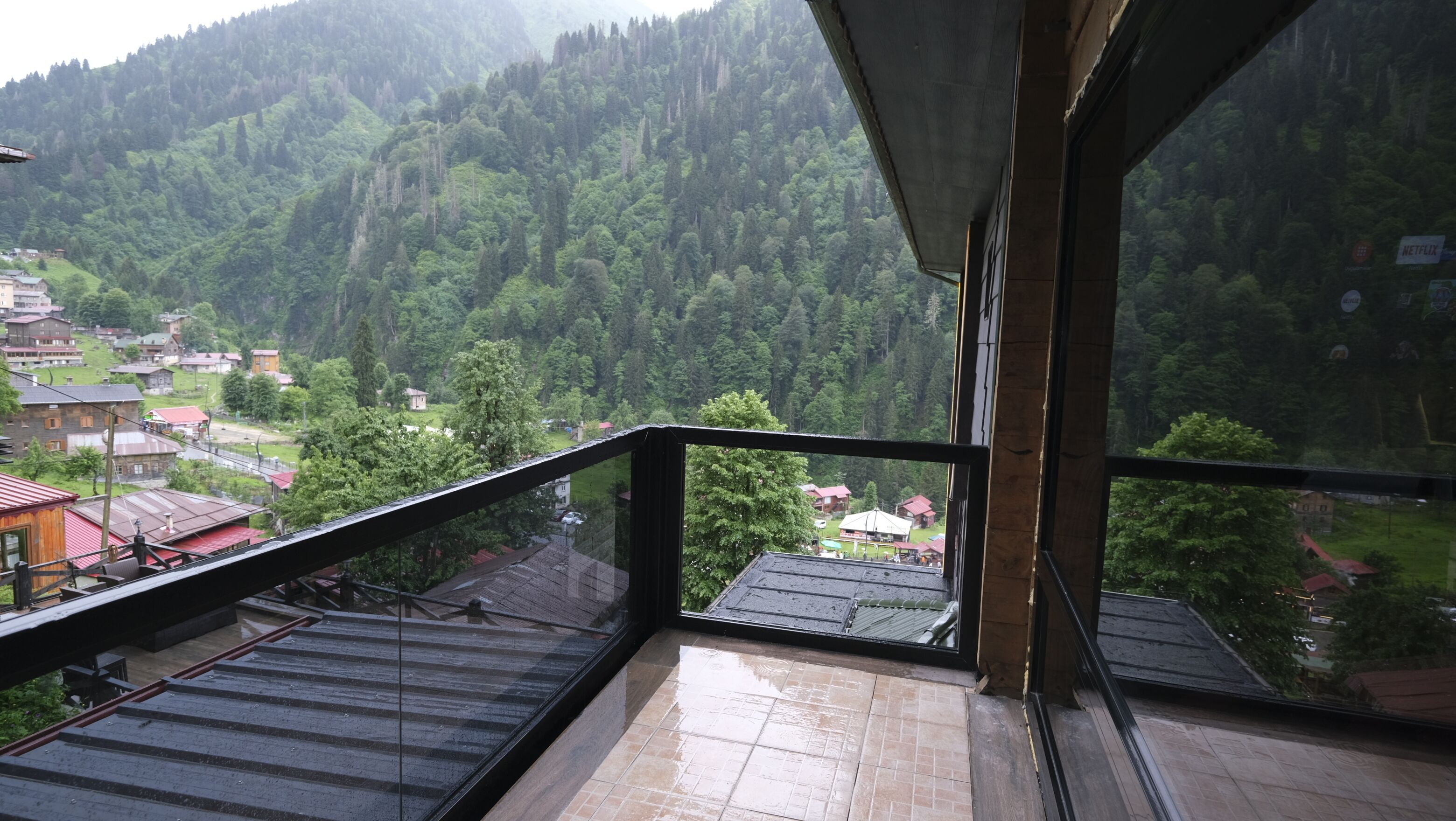 A balcony with a view of a forested valley and a small village below.