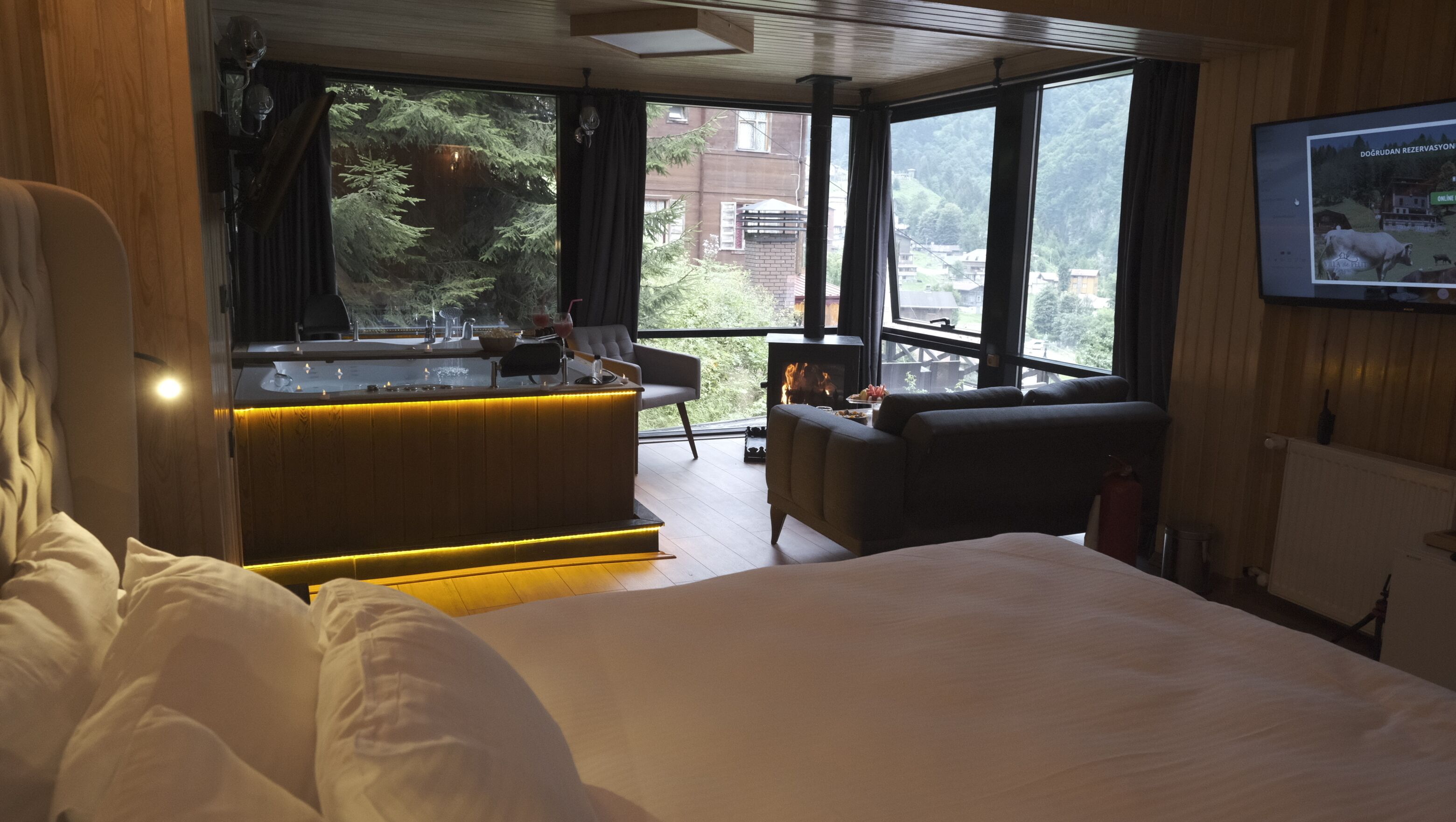 Une chambre d’hôtel moderne dotée d’un grand lit, d’un coin salon confortable, d’un bar avec vue et d’une cheminée.