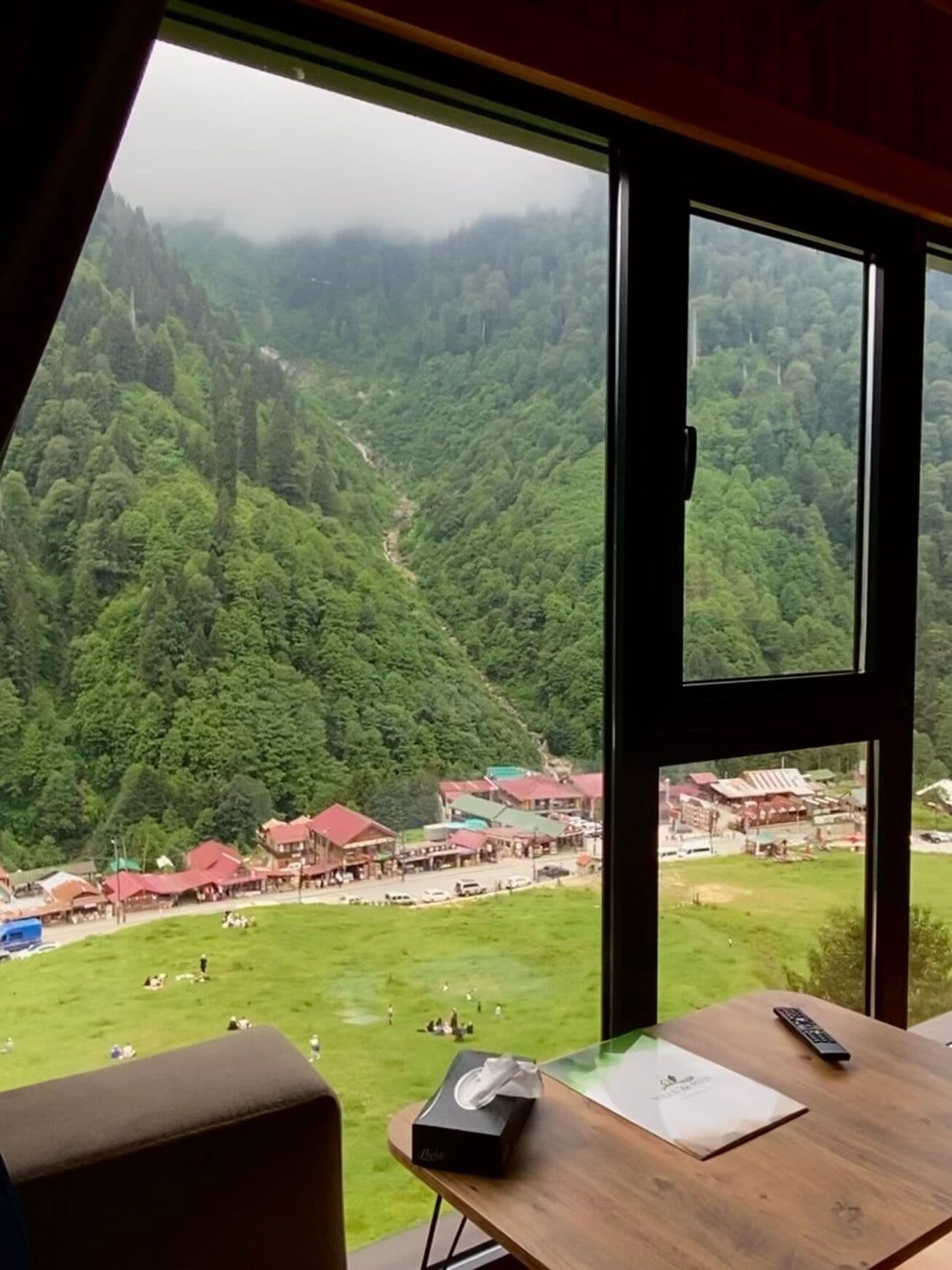 A room with a large window overlooking a mountainous landscape with a small village below.