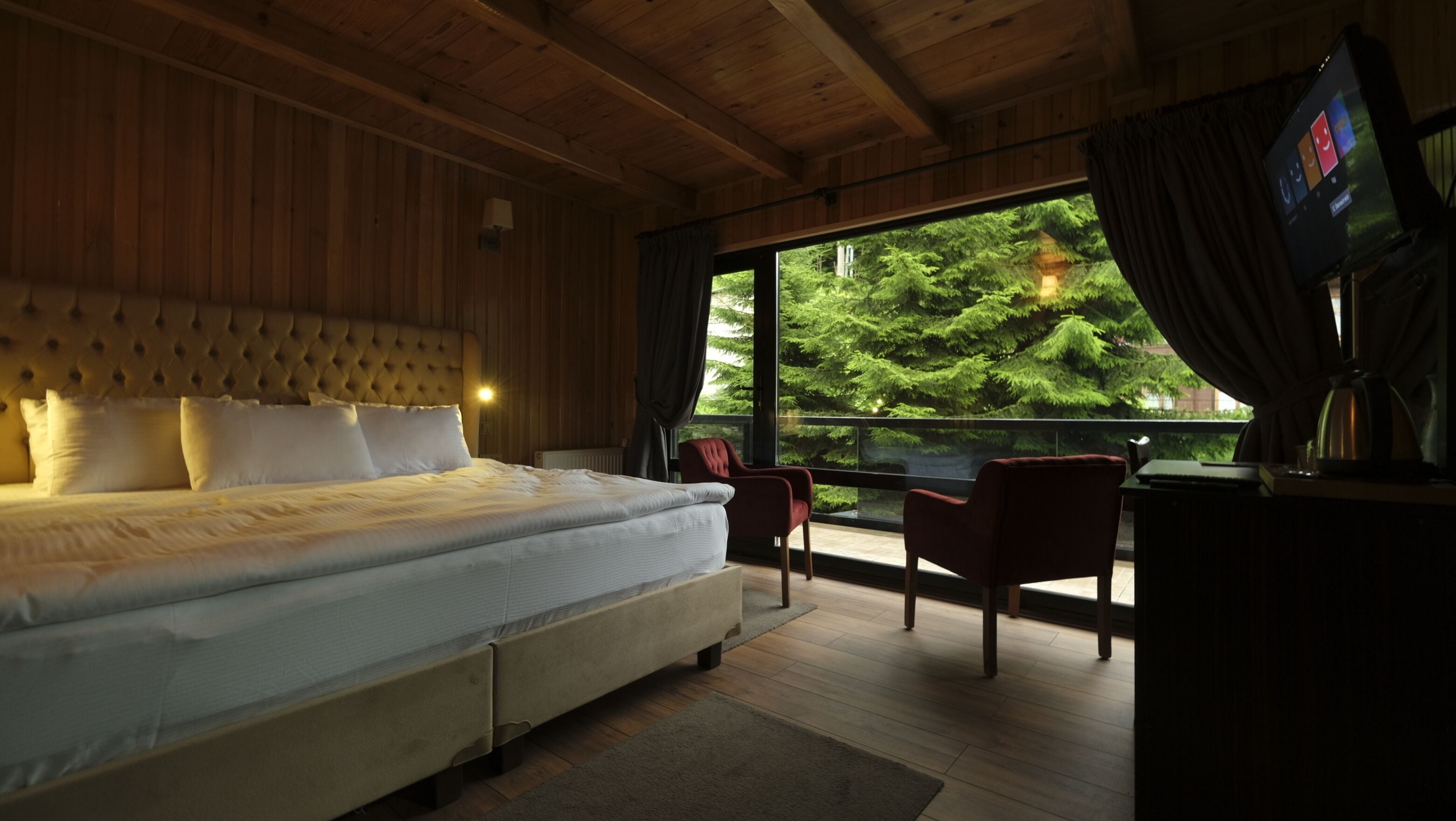 Un dormitorio con una cama grande, techo de madera y vista a un bosque por una ventana.