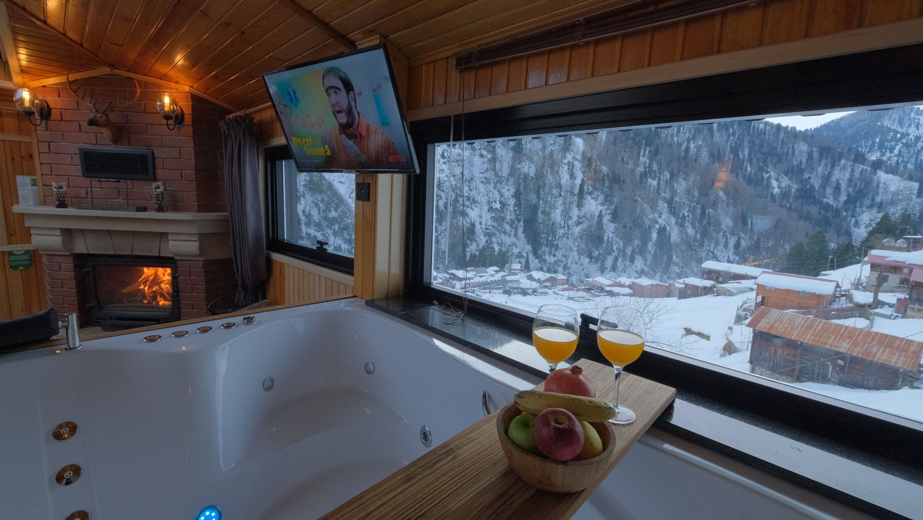 Een knus ingerichte kamer met een groot bad, een open haard en een televisiescherm waarop een film wordt afgespeeld.