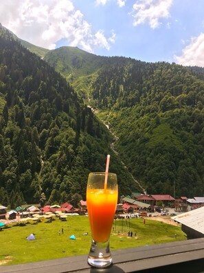 A glass of orange juice on a table with a mountain view in the background.