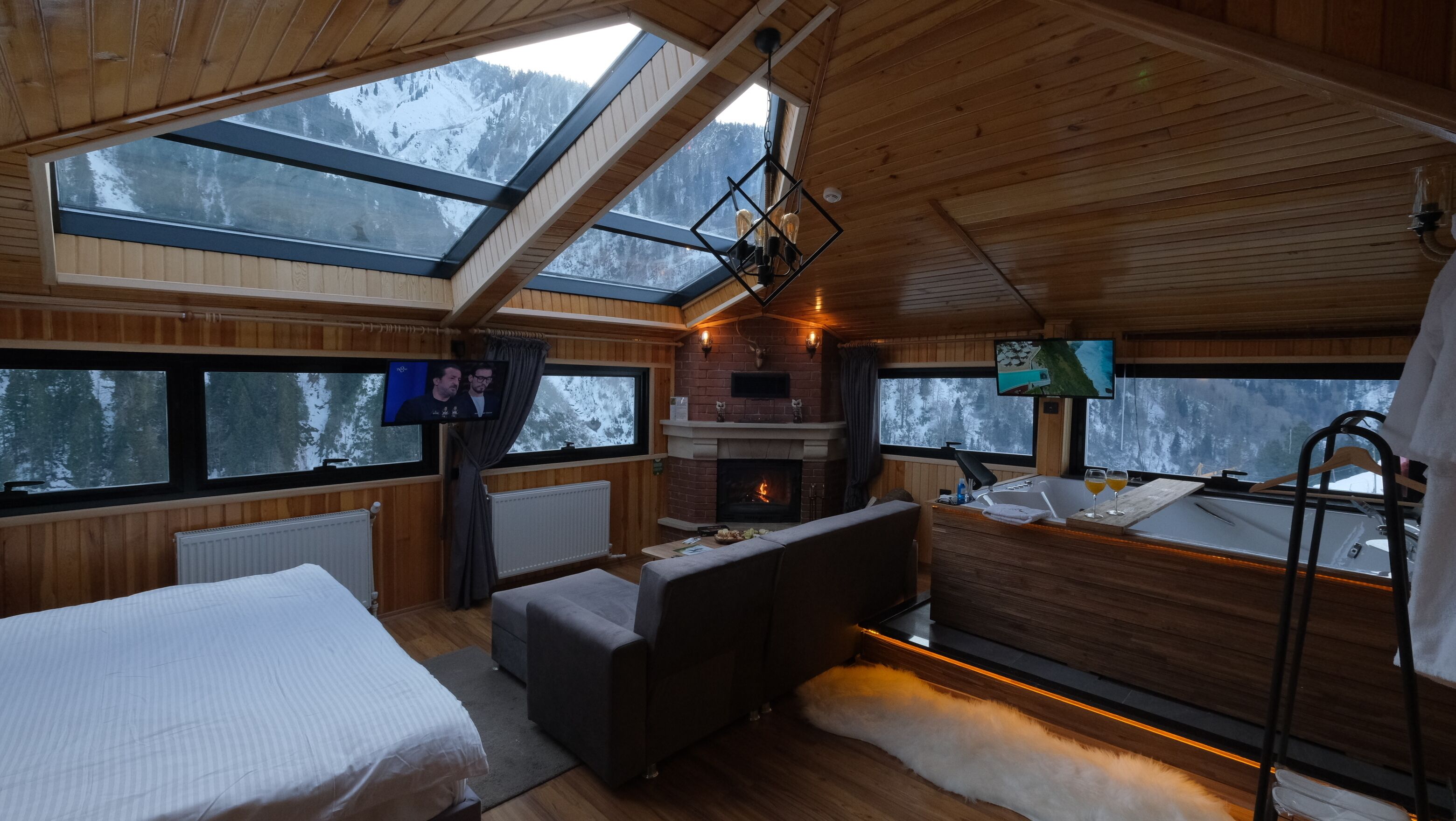 A cozy cabin with a fireplace, a TV, and a large window overlooking snowy mountains.
