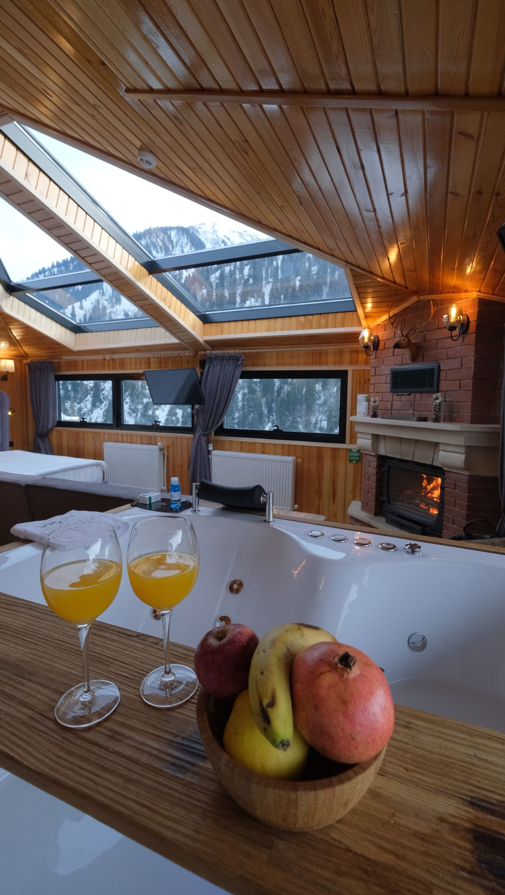 A cozy room with wooden ceilings, a fireplace, and a large window overlooking mountains.