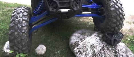 A vehicle with large tires and a rugged design, parked on a grassy area with rocks and a grill with food items.