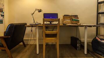 A small office space with a desk, a laptop, a chair, a lamp, and a shelf with books.