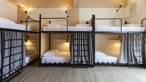 Quarto estilo dormitório com beliches, piso de madeira e iluminação fixada na parede.