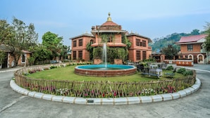 Un edificio grande con una fuente central, rodeado por un jardín circular con bancos.