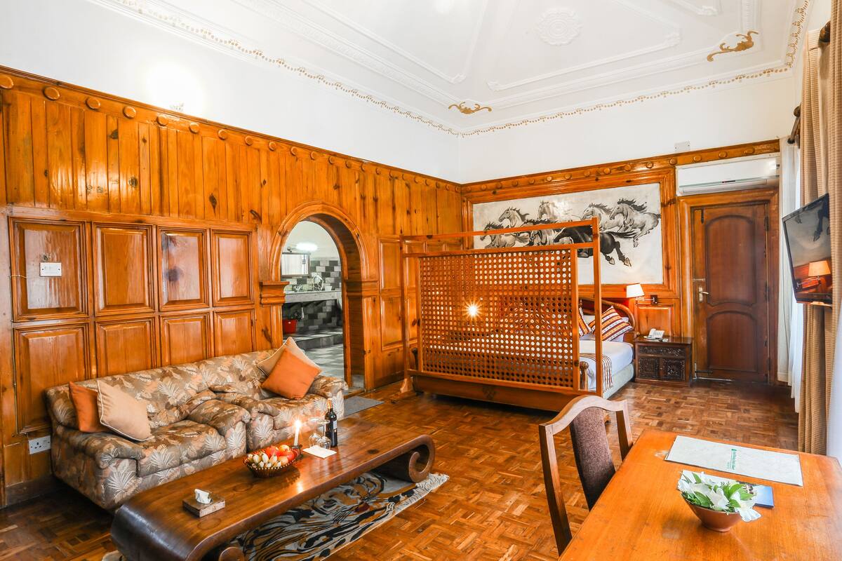 A room with a wooden panel wall, a sofa with cushions, a dining table with a bowl of flowers, and a wooden screen.