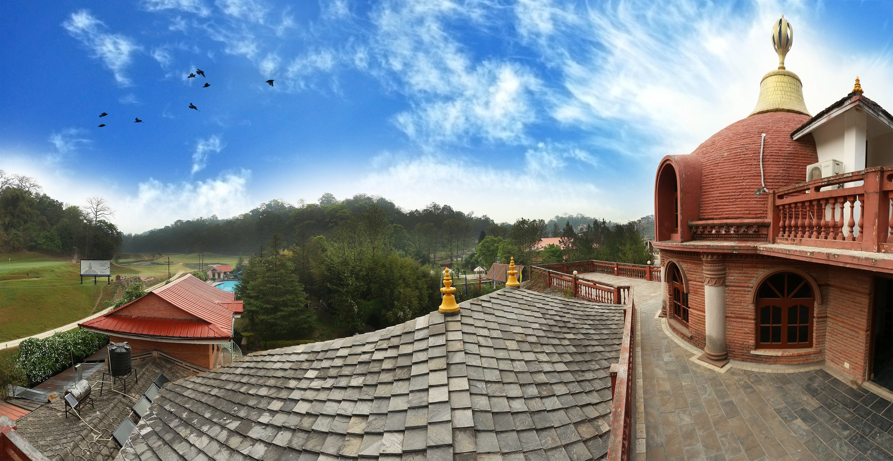 A building with a red roof and a dome structure, surrounded by greenery and a clear sky.