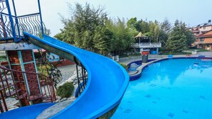 Una piscina con un tobogán azul, rodeada de árboles y edificios.