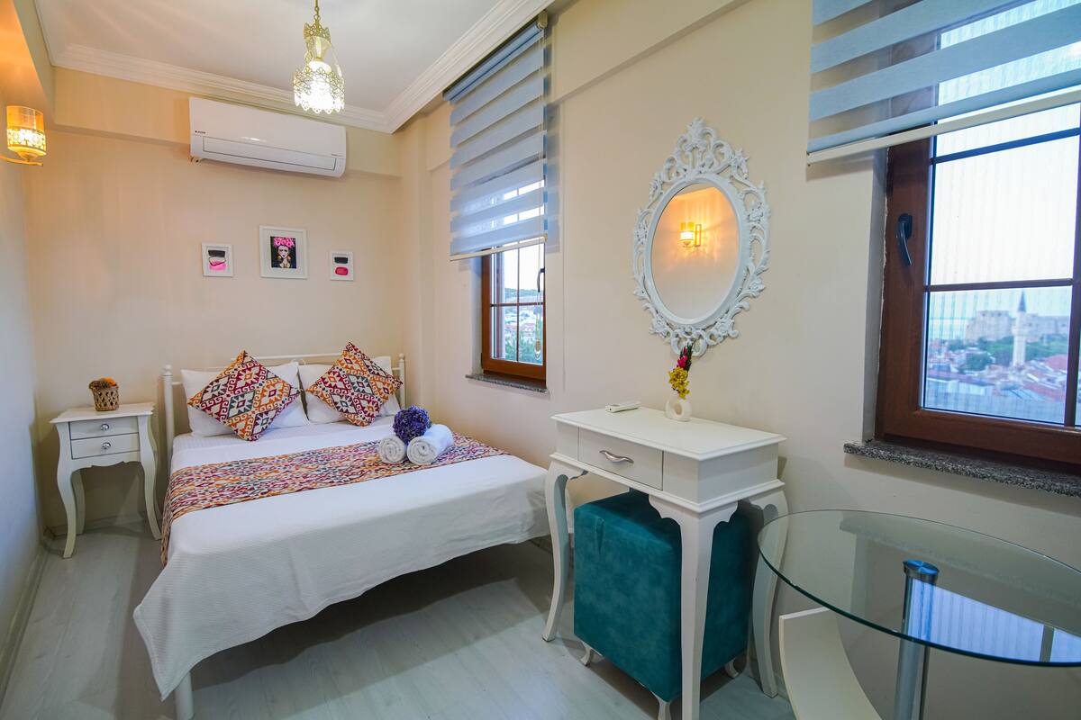 A hotel room with a bed, bedside table, dresser, and a large mirror.