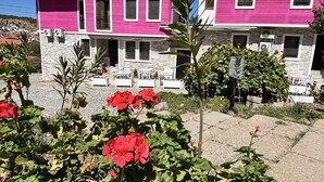 Een roze huis met zonnepanelen, een stenen muur en een tuin vol rode bloemen.
